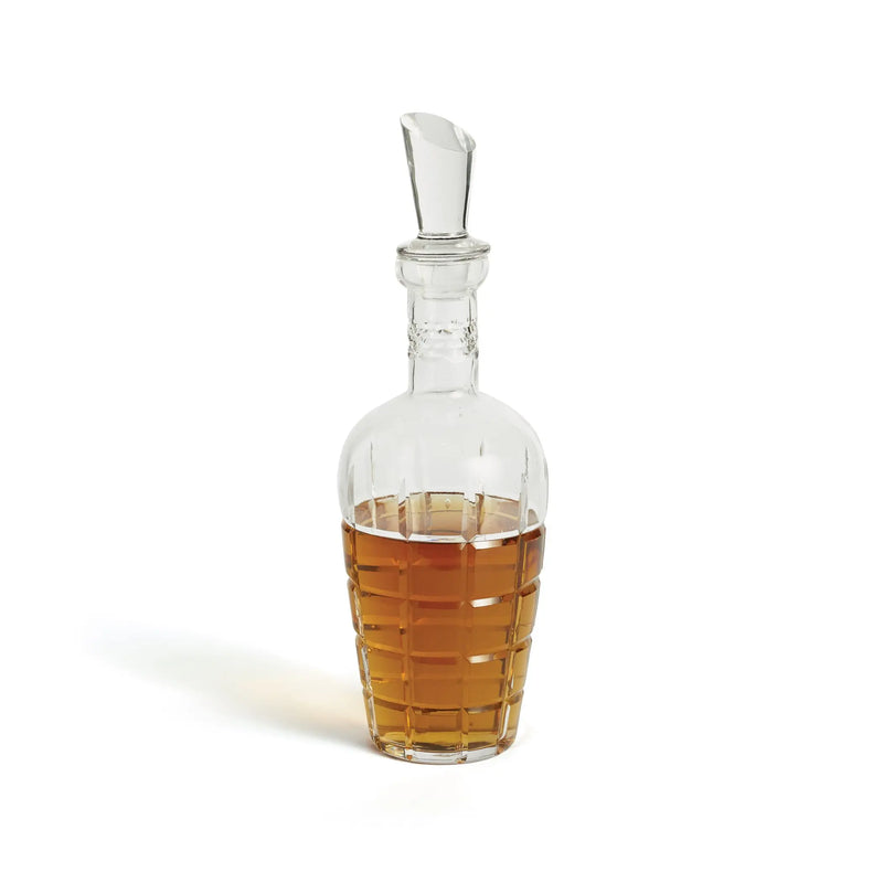 Glass decanter with a silver stopper filled with amber liquid on a white background