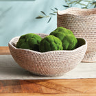Woven off-white bowl with scalloped edge with green moss balls inside on a wooden table with blue wall behind