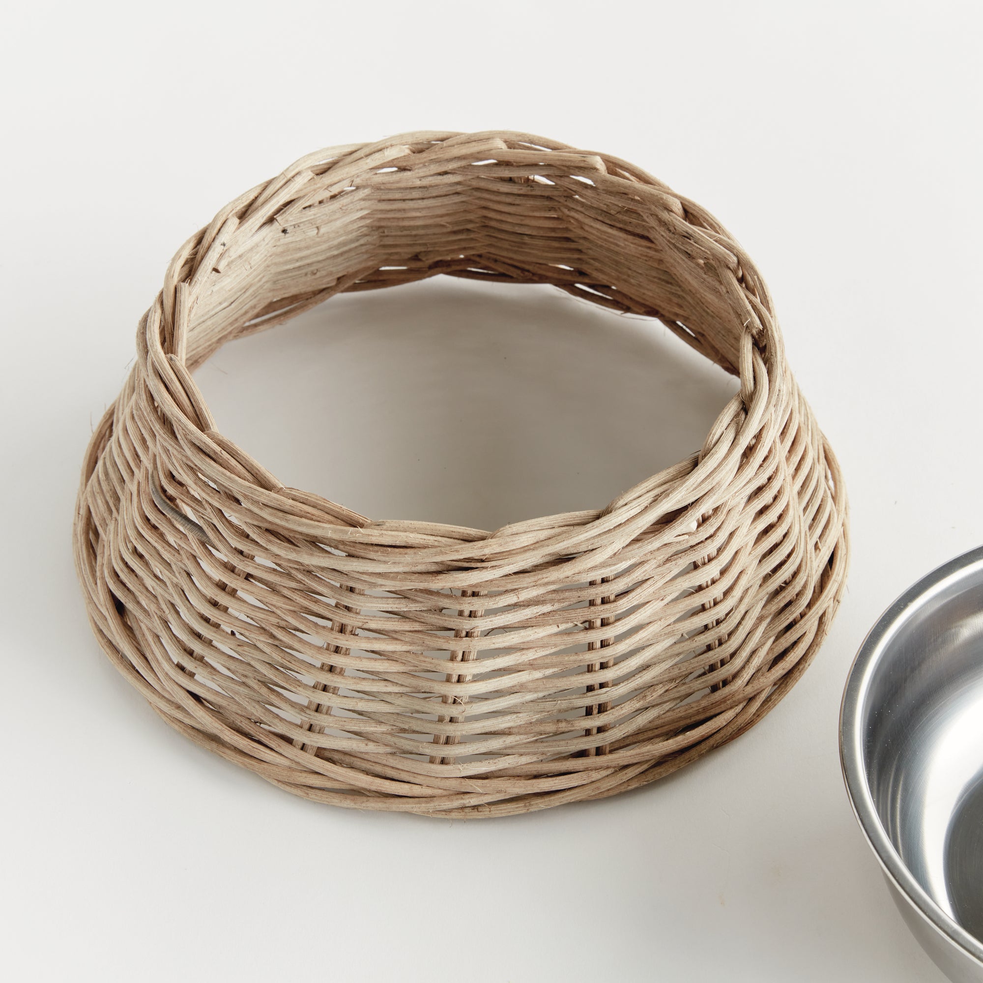 Wicker dog bowl with stainless steel insert on white background