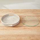 Round woven tray with handles and glass insert sitting separately on wooden table