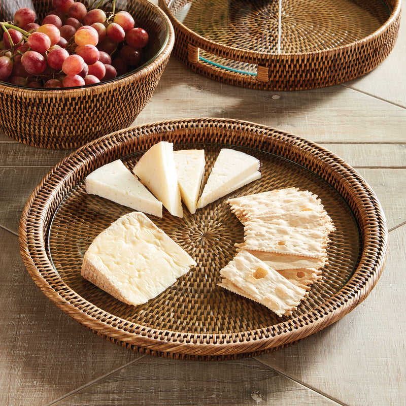 Circular rattan tray with glass insert with cheese and crackers on wood table