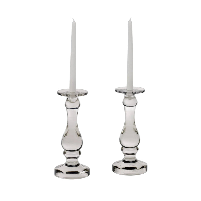 Two clear glass candlesticks with white candles on a white background