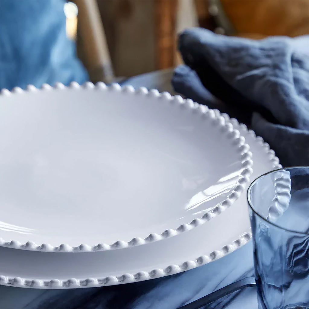 White ceramic plate with decorative edge on a blue cloth with a glass beside it.