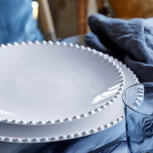 White ceramic plate with decorative edge on a blue cloth with a glass beside it.