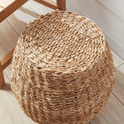 Woven brown cube stool on white porch  with wood floor next to a wooden chair