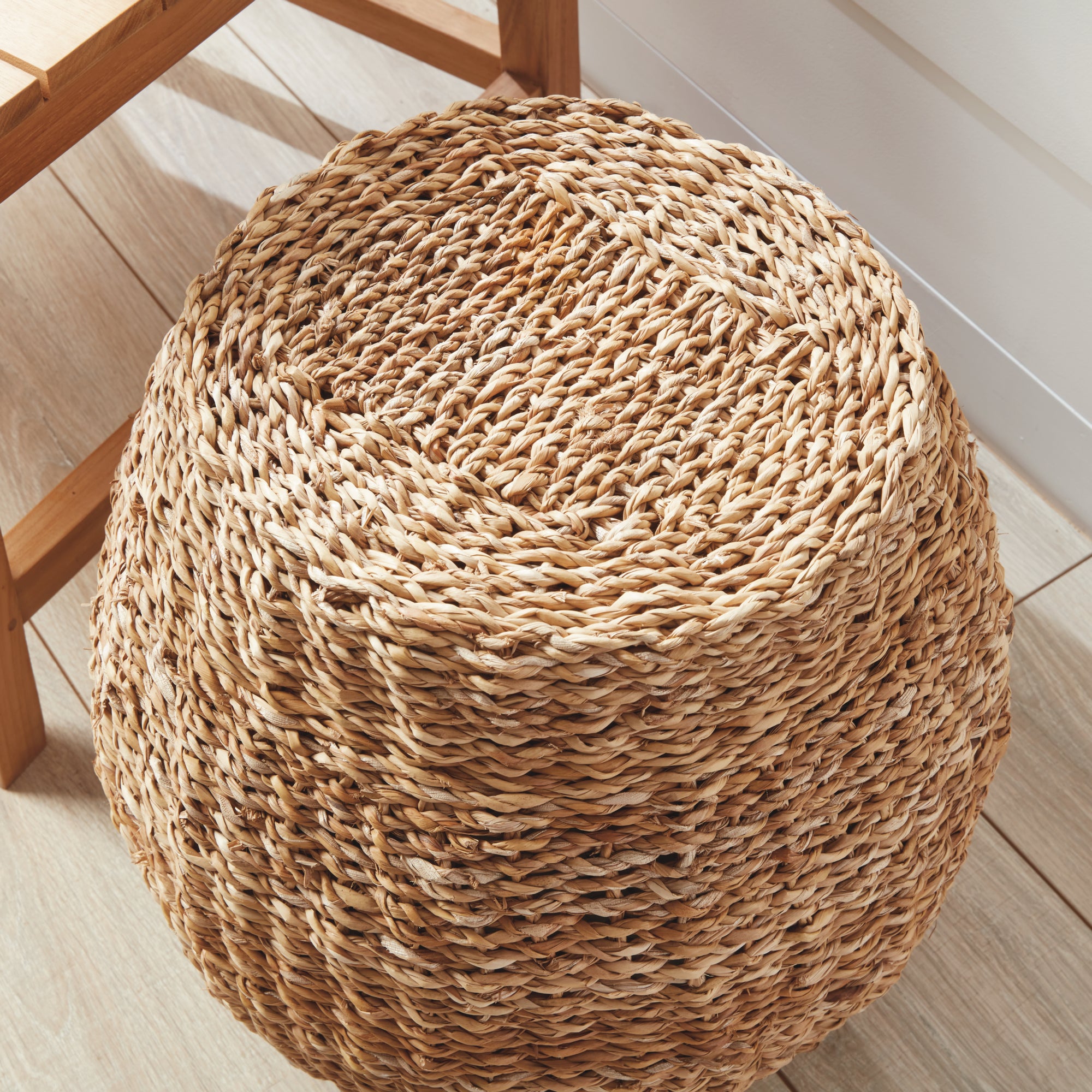 Woven brown cube stool on white porch  with wood floor next to a wooden chair