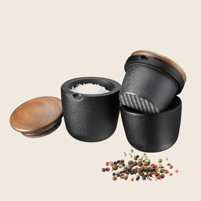 Set of black salt and pepper shakers with wooden lids on a beige background