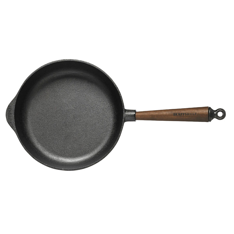 Black cast iron skillet with wooden handle on beige background
