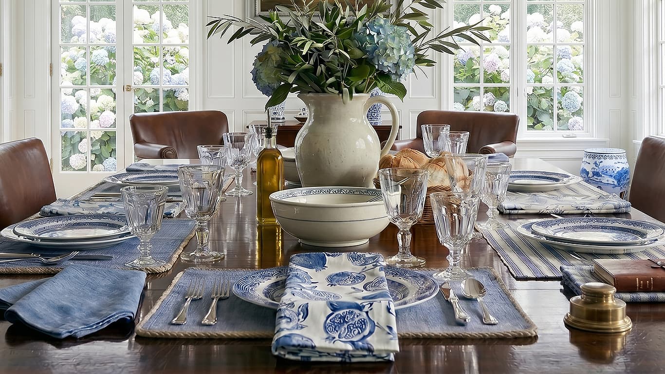 Elegant dining table setting with floral centerpiece, plates, and glasses in a bright room.
