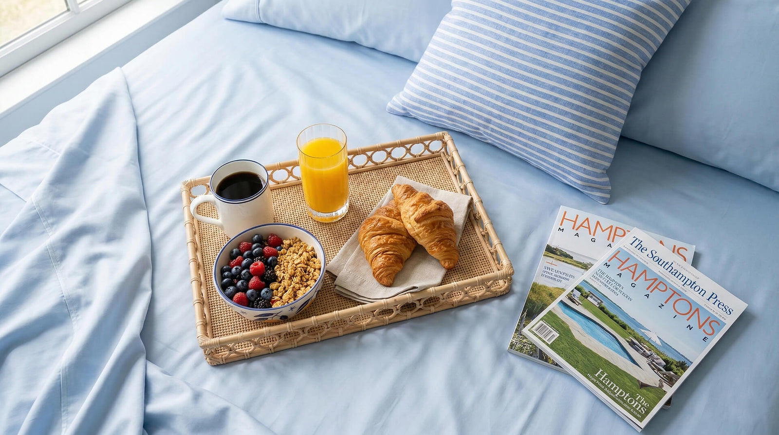 Breakfast tray with croissants, cereal, berries, and coffee on a bed with newspapers.