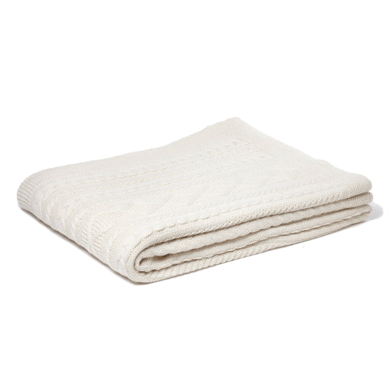 A folded beige cable knit throw made of baby alpaca wool.