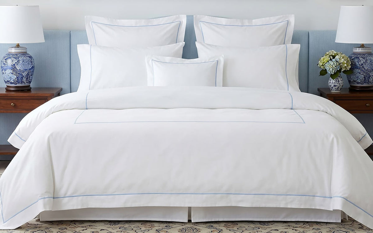 White bedding set with blue piping on a bed in a bedroom setting.