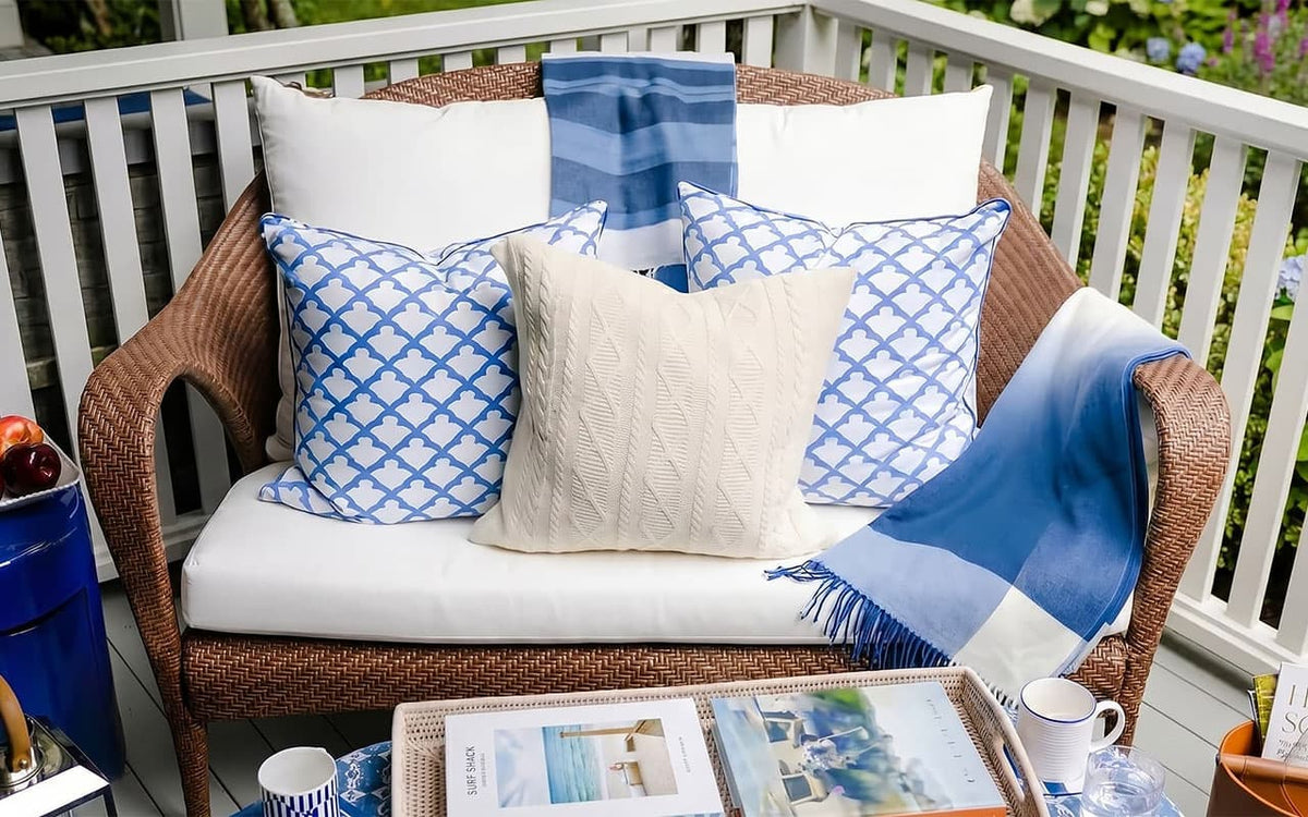 Wicker chair with blue and white patterned cushions and a blanket on a patio.