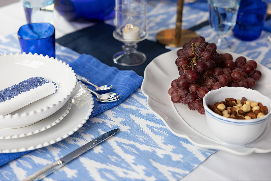Dining table setting with grapes, nuts, and cutlery on a blue and white patterned tablecloth.