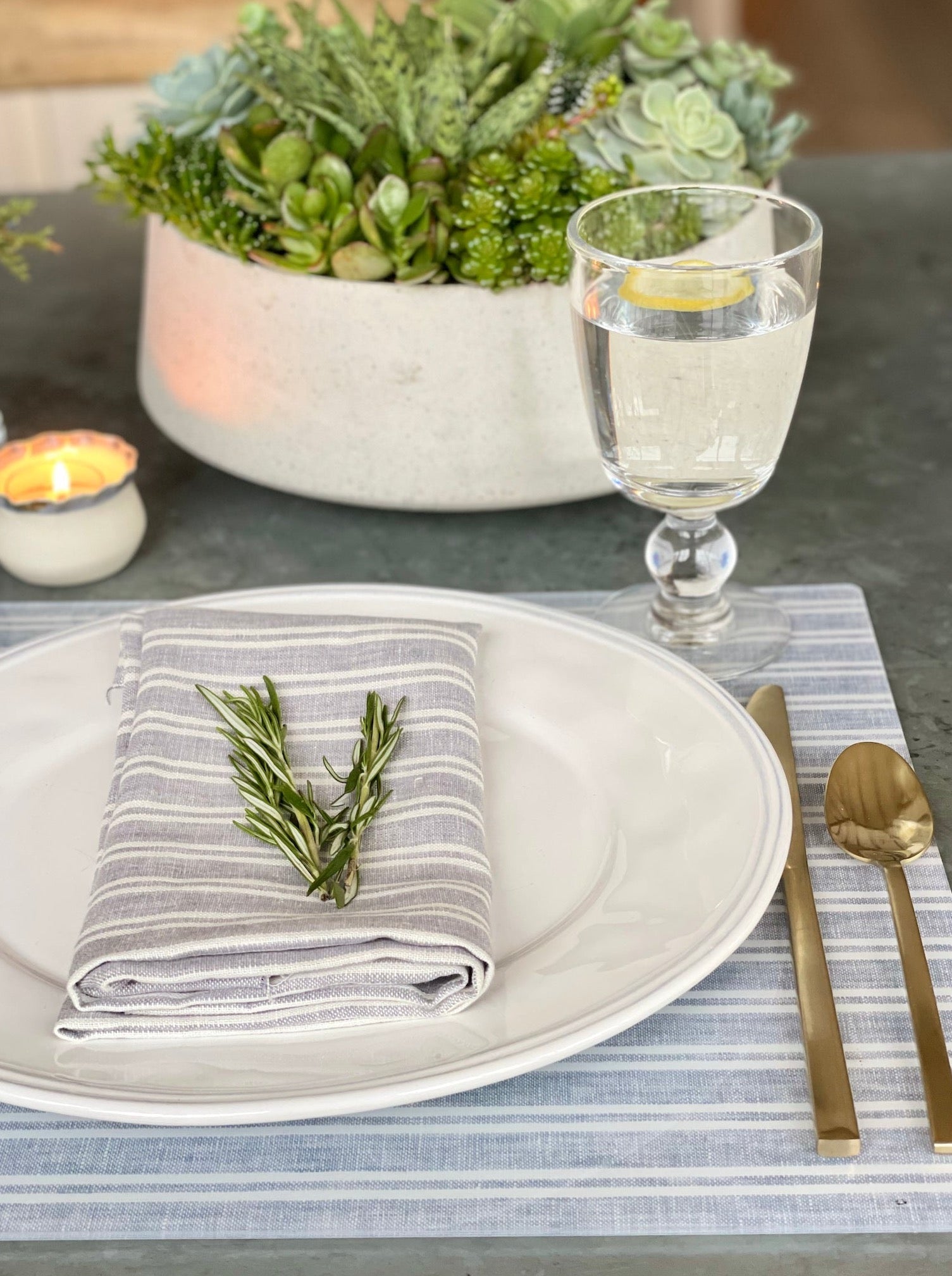 Table setting with a plate, napkin, and glass on a striped placemat.