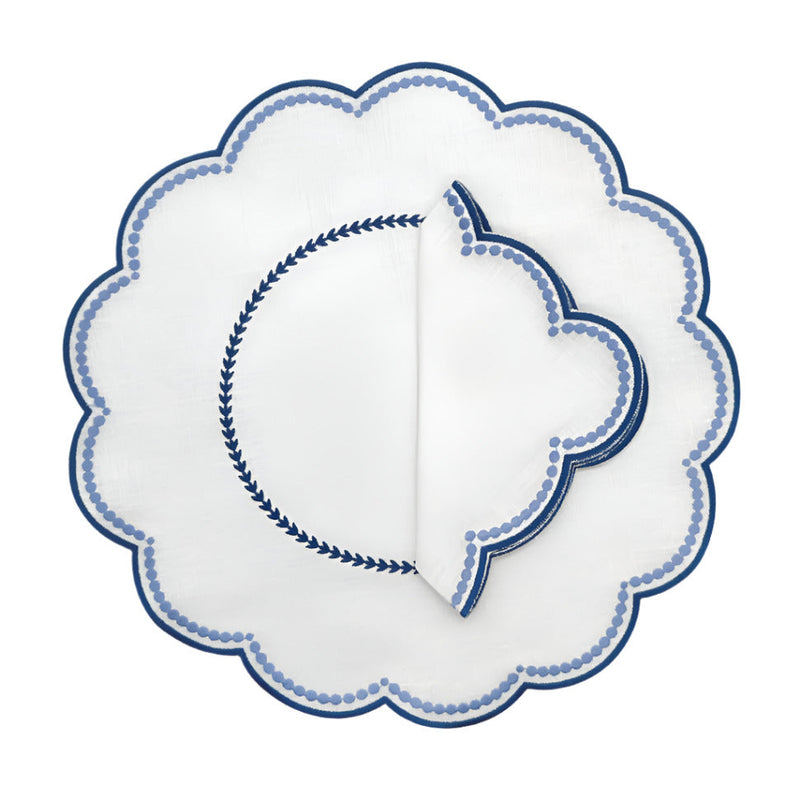 A set of four round placemats with blue scalloped edges and embroidered details in the center.