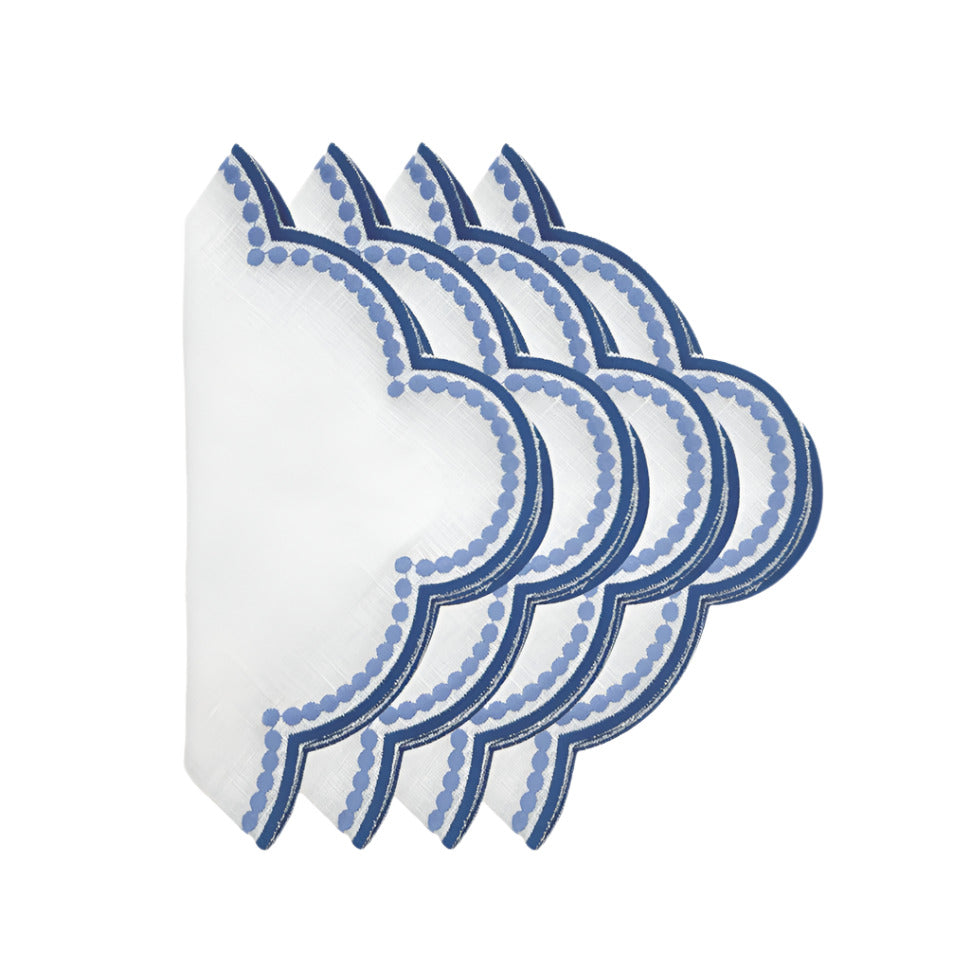 A set of four folded white linen napkins with a blue floral pattern.