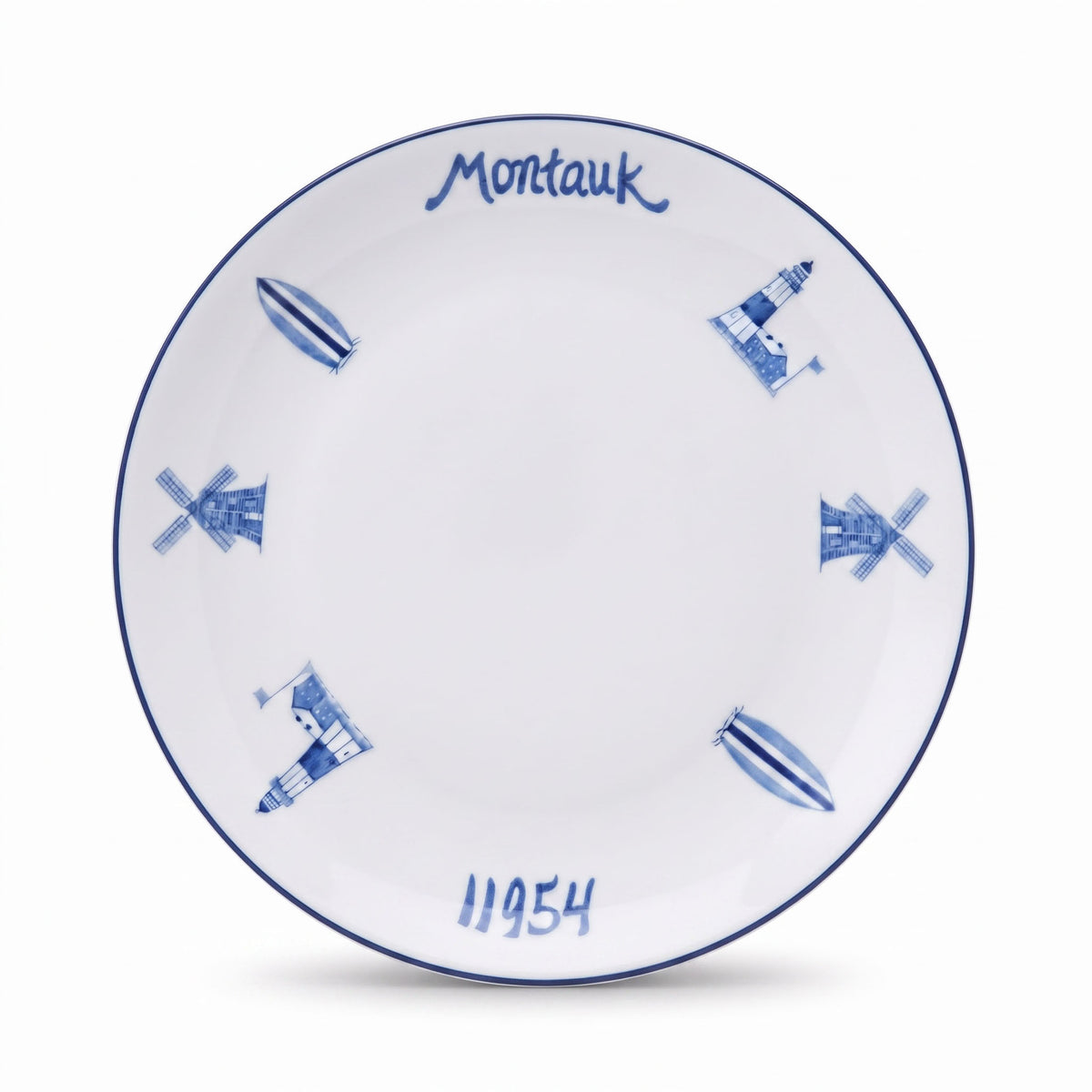 A white ceramic plate with a blue hand-painted design, featuring the brand name 'Montauk' at the top, blue windmills and lighthouses, the year '1954' at the bottom, and a blue rim.
