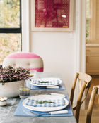 Dining table set with plates, napkins, placemats and glasses in a bright room.