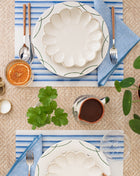 Table setting with white floral plates, blue striped napkins, and a cup on a textured surface.
