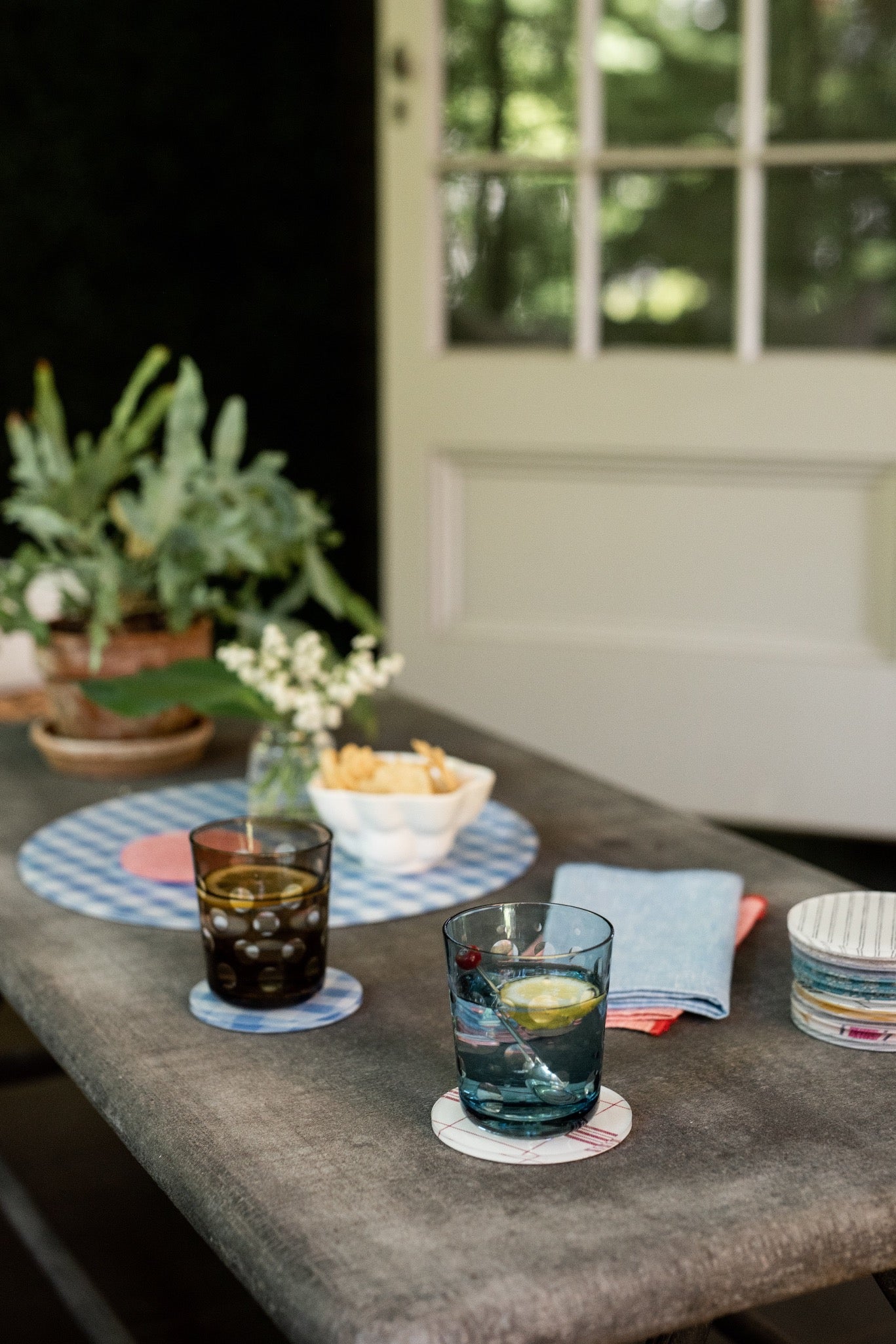 Outdoor setting with drinks on a table with coasters, plants, and a door in the background