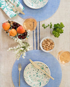 Table setting with blue plates, gold cutlery, placemats and small dishes of fruit and nuts.