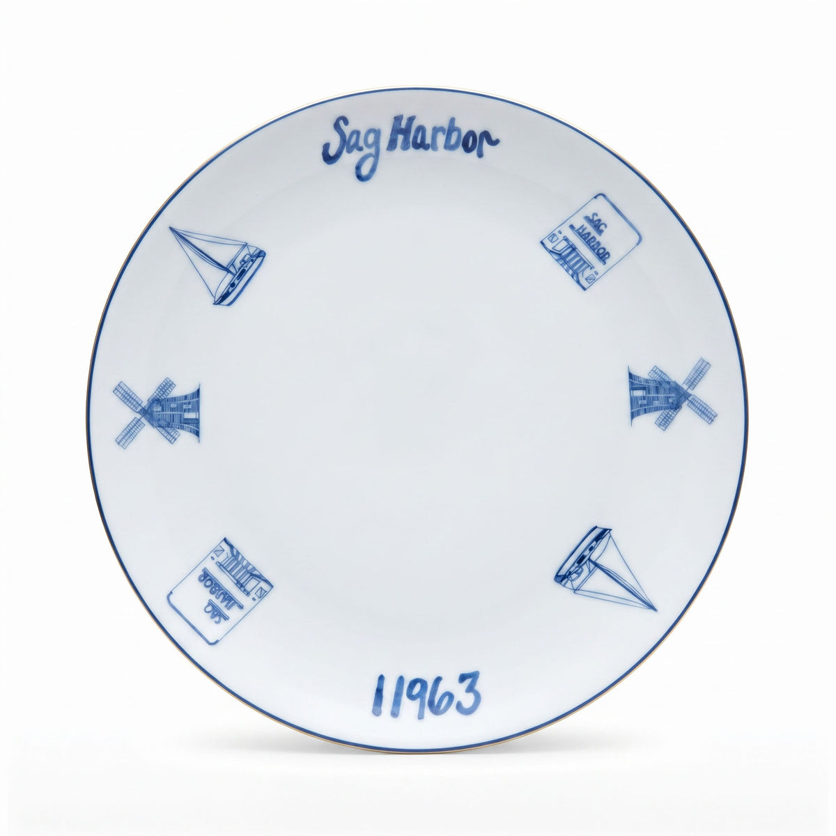 A white ceramic plate with blue hand-painted illustrations of sailboats, windmills, and stamps, featuring the text 'Sag Harbor' and '11963'.