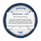 A circular decorative plaque or coaster featuring a blue and white Southampton design with a textured navy blue outer ring, a gold glitter inner ring, and a white center with printed text reading 'Southampton - 11968' and descriptive copy about Hampton Elegance.