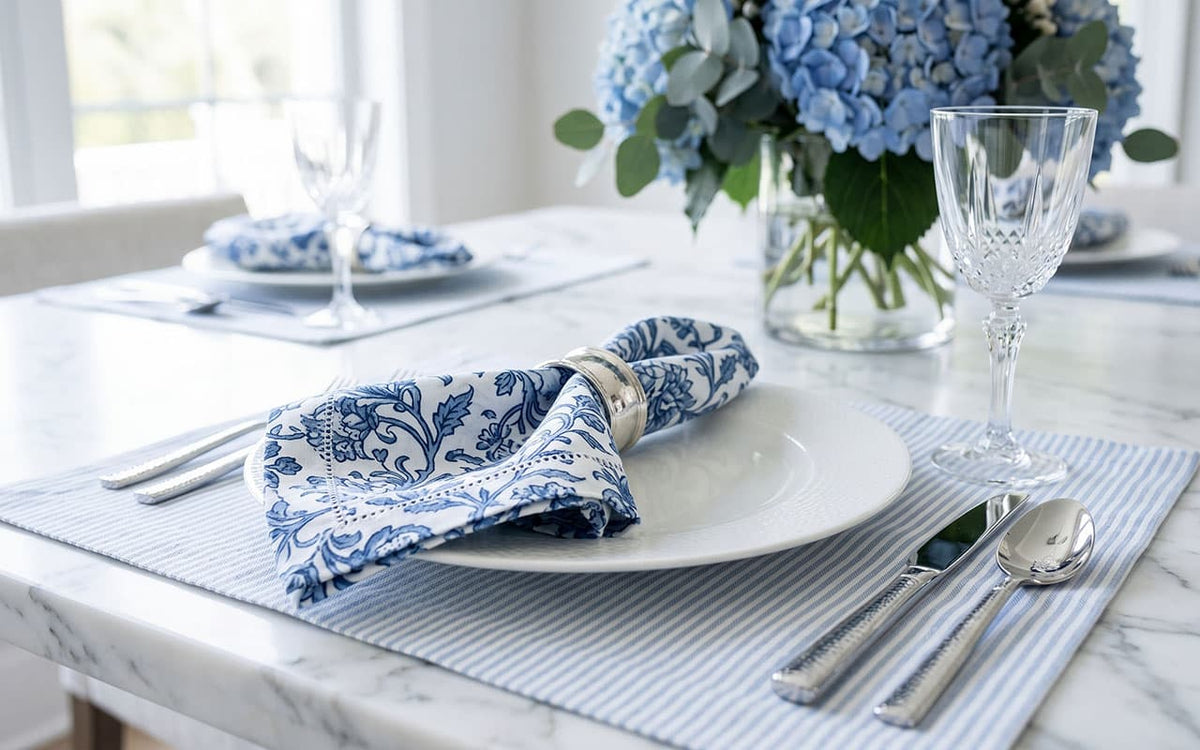 Elegant table setting with blue and white napkins, glasses, and a vase of flowers.