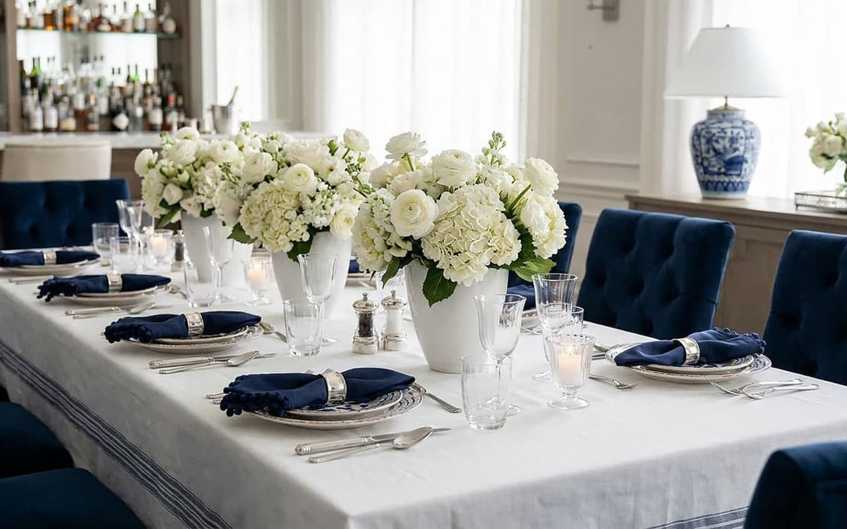 Elegant dining table setting with white flowers, silverware, and blue napkins.