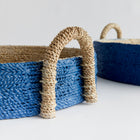 Close up of two seagrass basket trays with blue outside on white background.