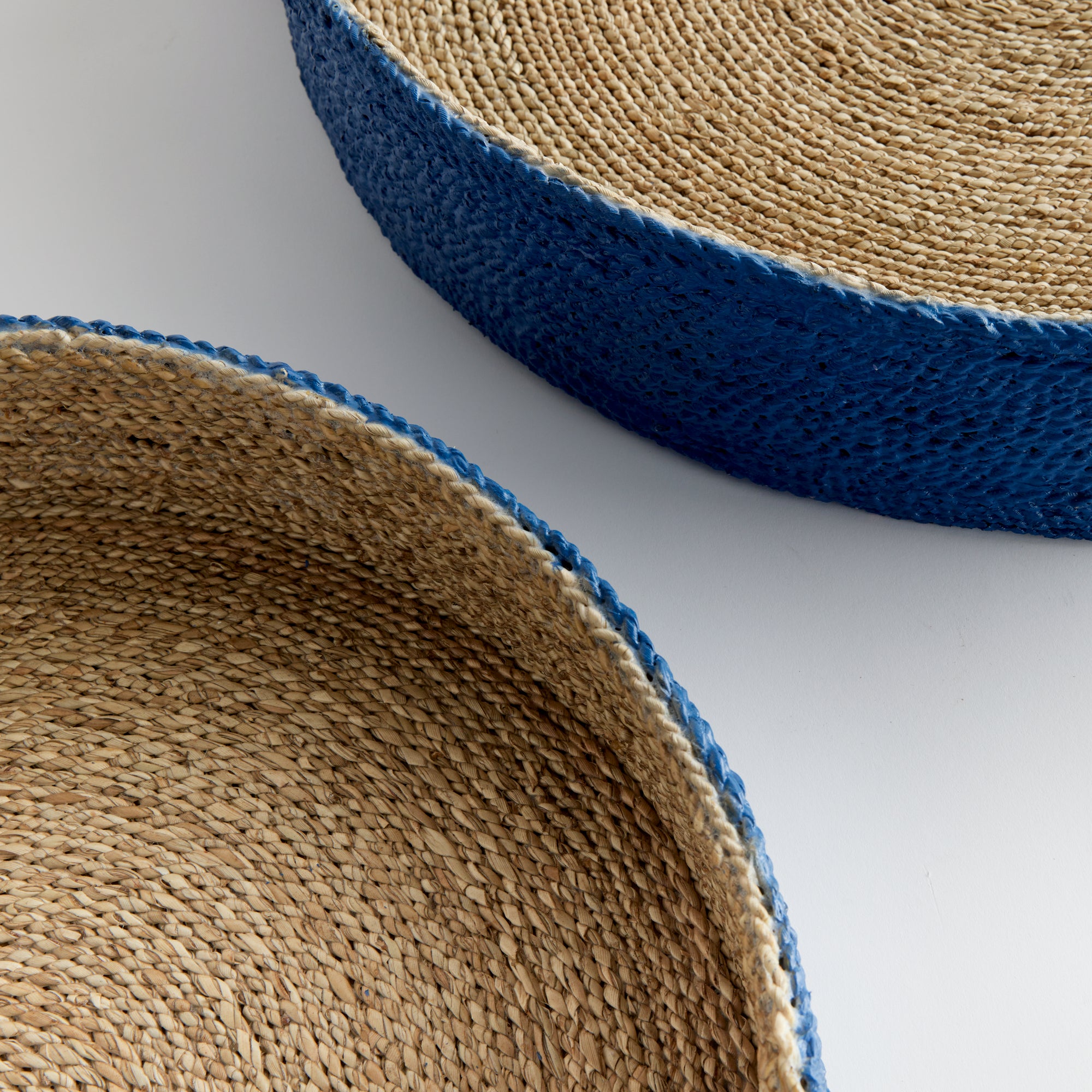 Close up of two seagrass basket trays with blue outside on white background.