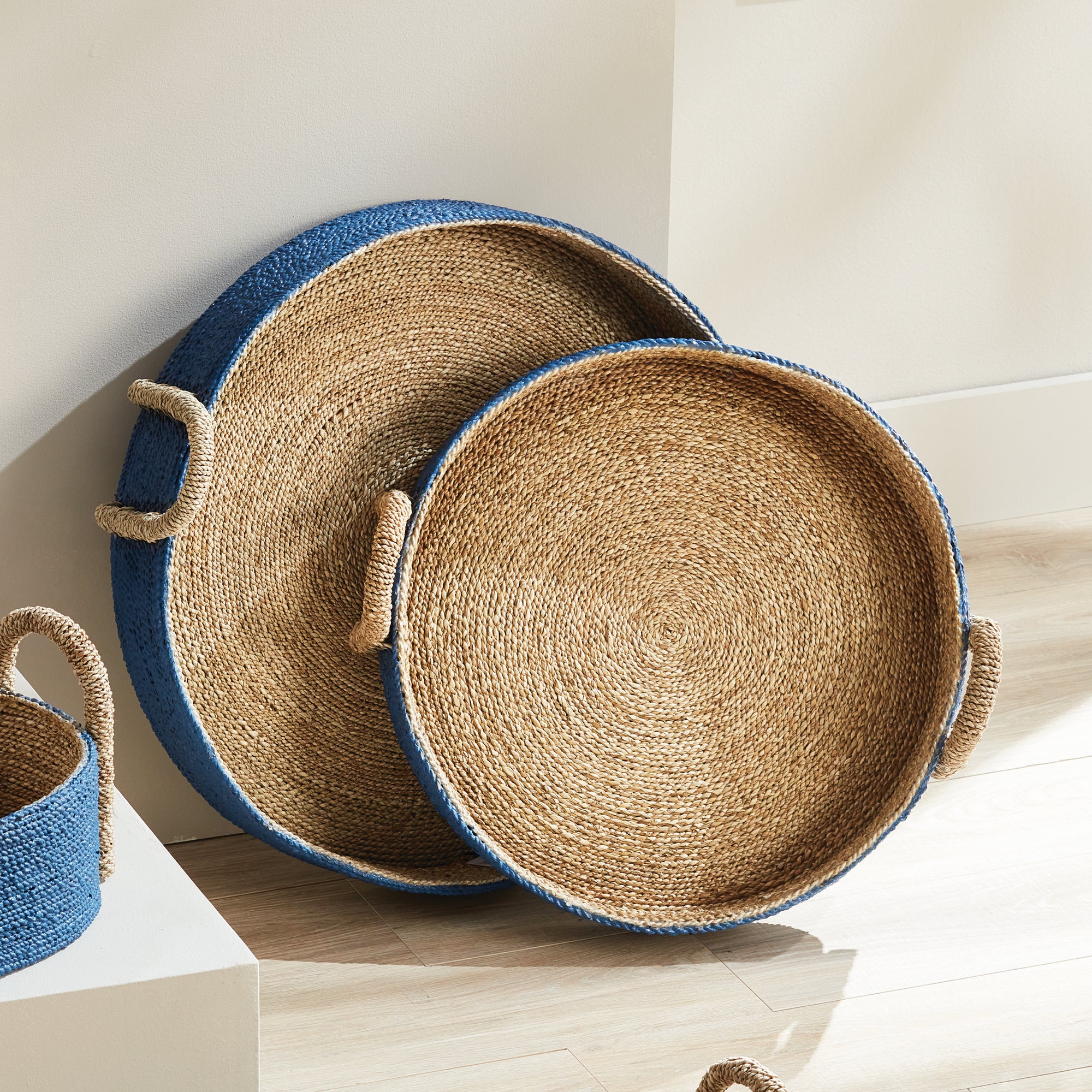 Two seagrass basket trays with blue outside on white background.