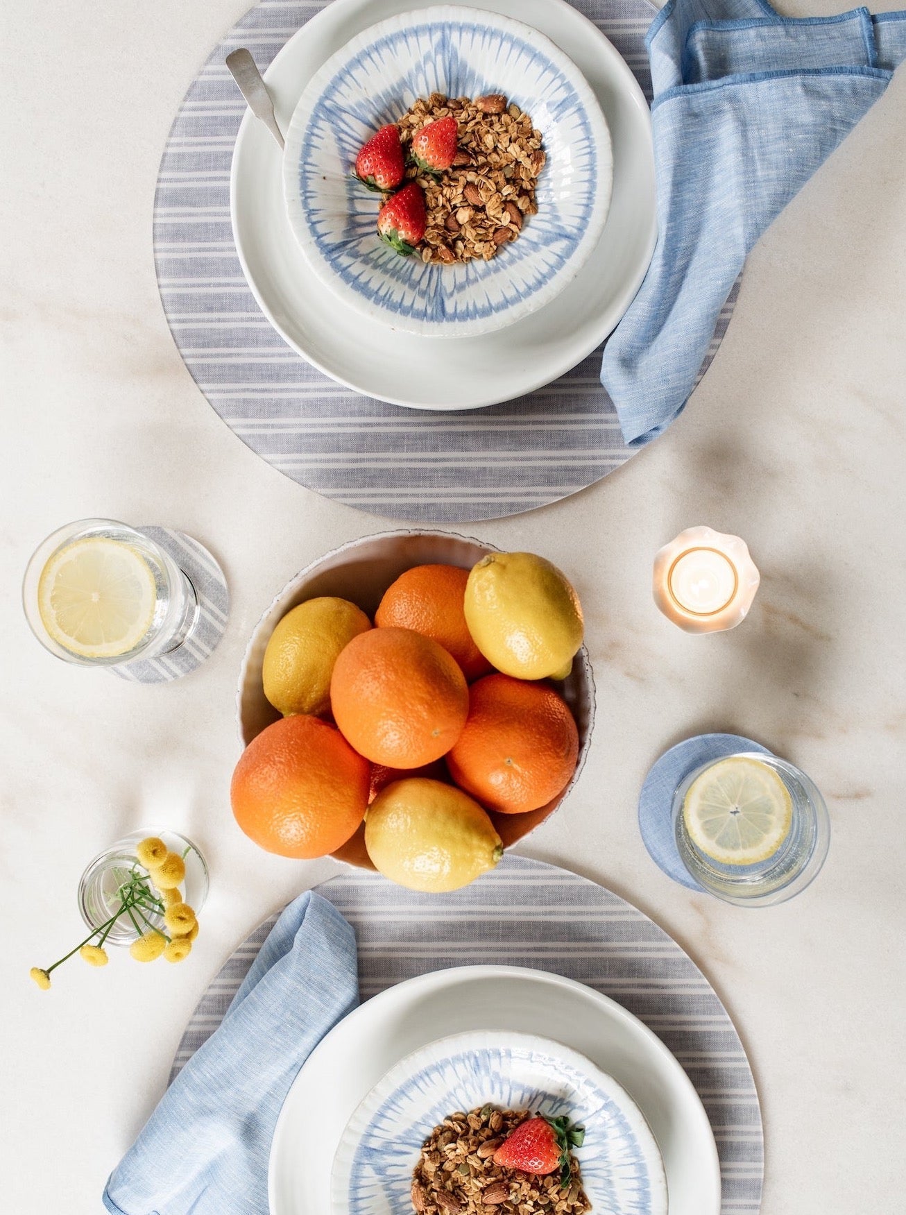Table setting with bowls of granola and fruit, glasses of water, and a candle.